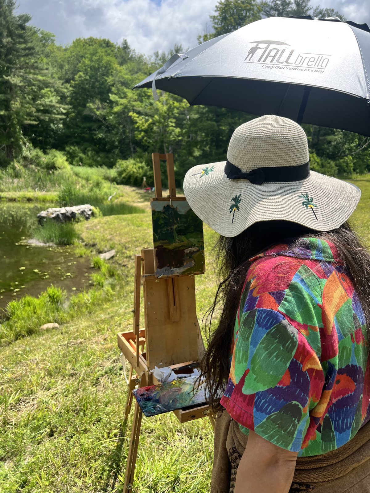 A painting by Elena Rykoff in progress on an easel beside the pond