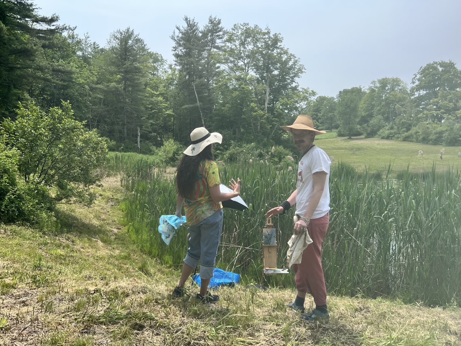 Kristin teaching a student at an easel beside tall grasses